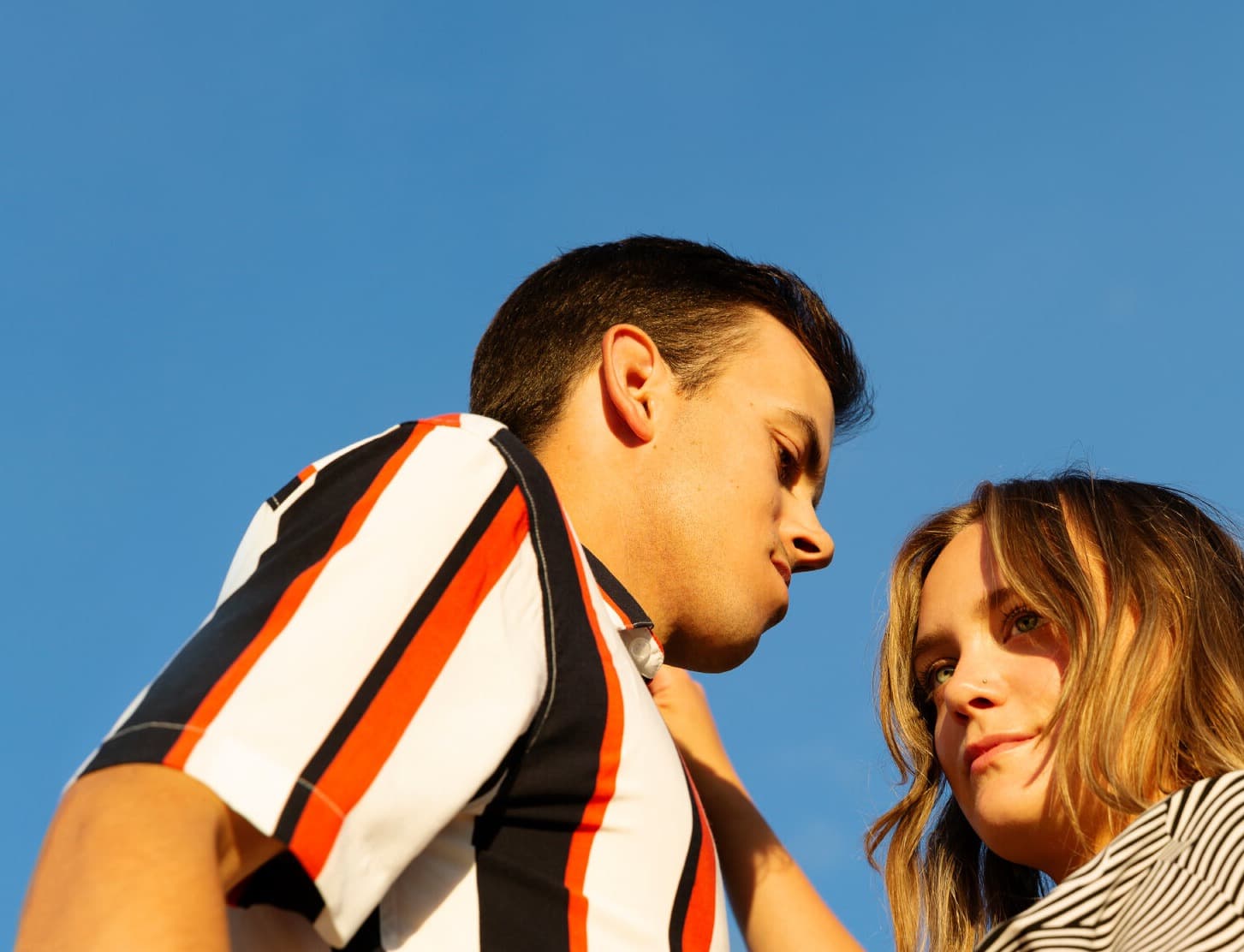 Image looking up at the two members of Post Script. They stand in front of a blue sky and both are wearing striped shirts.