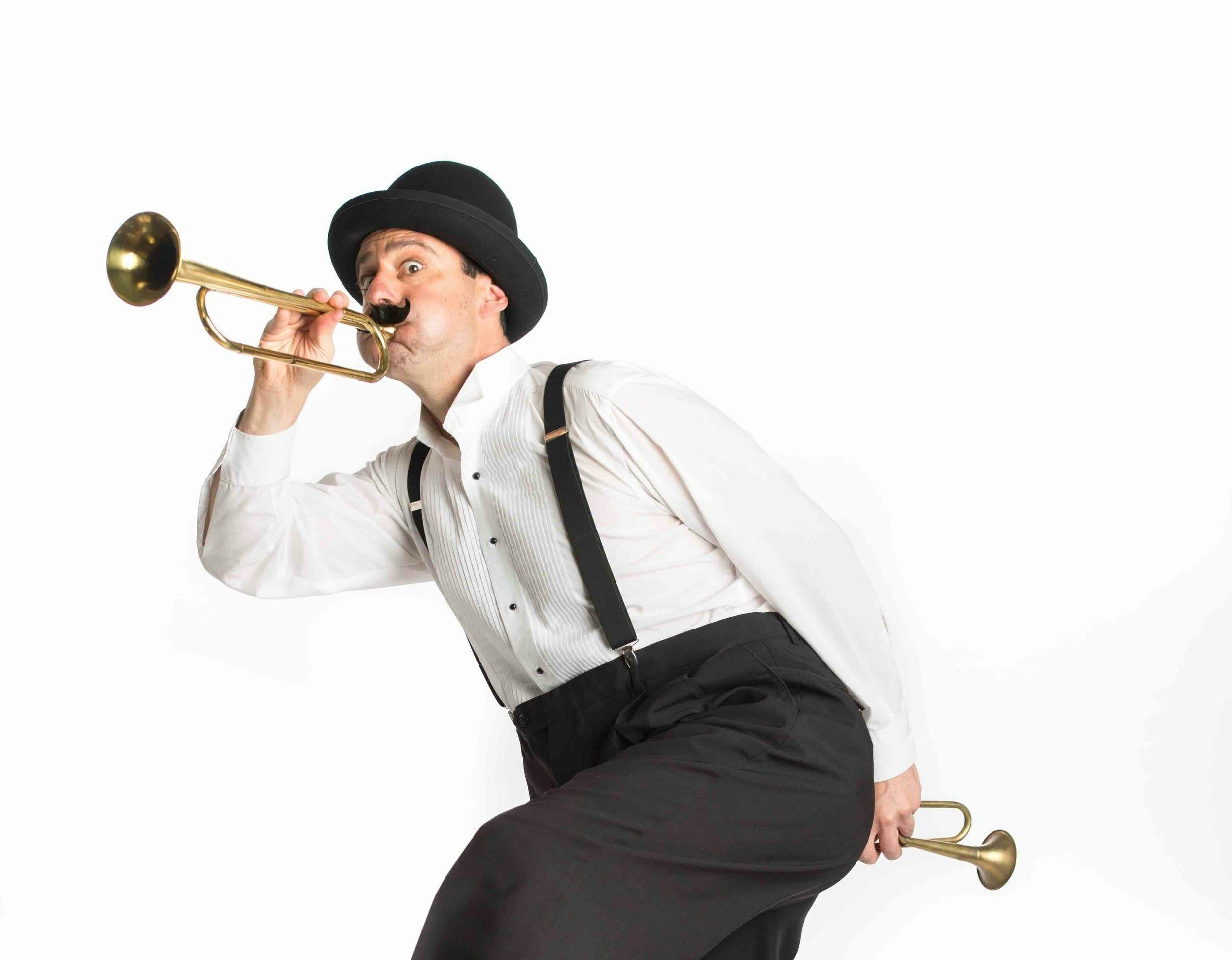 A silly image of Aytahn Ross in a white collared shirt, black suspenders, and holding two trumpets - one at his lips and one pointed away from his butt. He has a goofy expression on his face.